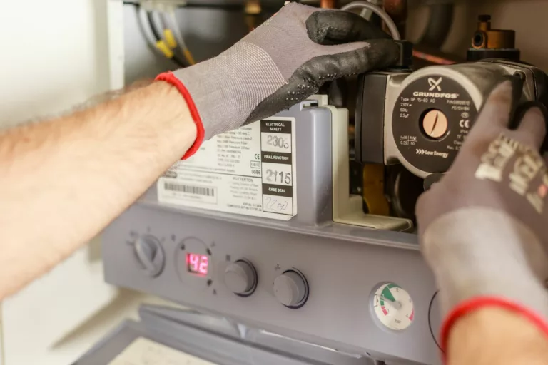 Objectif PEB 2033 à Bruxelles : remplacer la chaudière suffit-il pour améliorer le certificat du logement ? Close-Objectif PEB 2033 à Bruxelles : remplacer la chaudière suffit-il pour améliorer le certificat du logement ? of hands adjusting a boiler system with precise instrumentation, showing maintenance work.