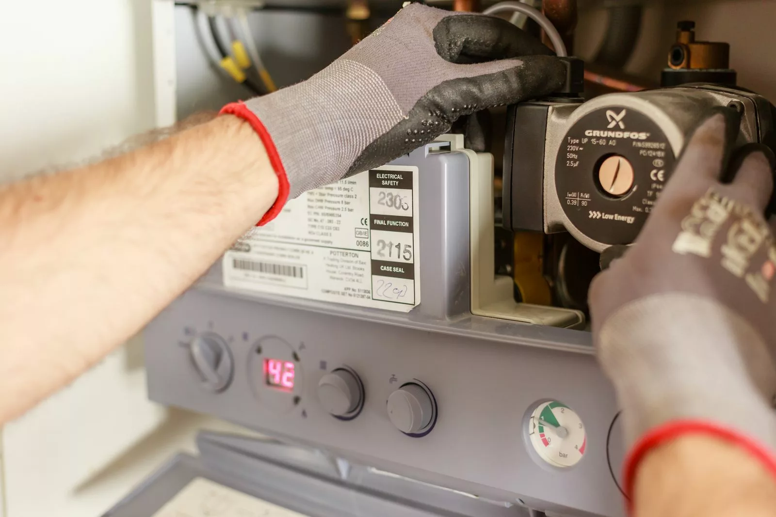 Close-Objectif PEB 2033 à Bruxelles : remplacer la chaudière suffit-il pour améliorer le certificat du logement ? of hands adjusting a boiler system with precise instrumentation, showing maintenance work.